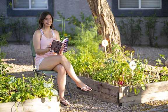 A woman is sitting on a chair in a garden, reading a book.