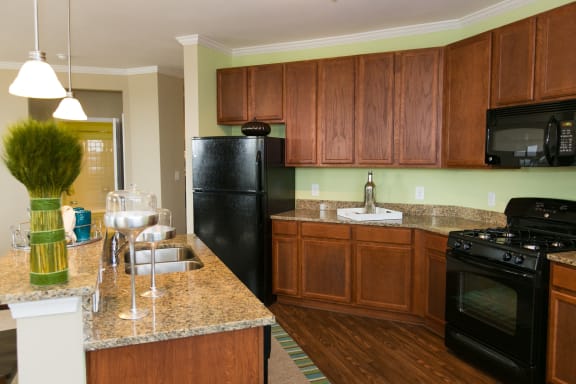 kitchen at VistaView apartments in Frederick, MD with black appliances, dark wood cabinets and flooring, kitchen island with sink and counter seating and stone countertops at VistaView, Frederick
