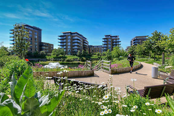A person is walking in a park with tall buildings in the background.