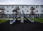 Thumbnail 5 of 8 - A playground with a slide and a climbing frame in front of a building.