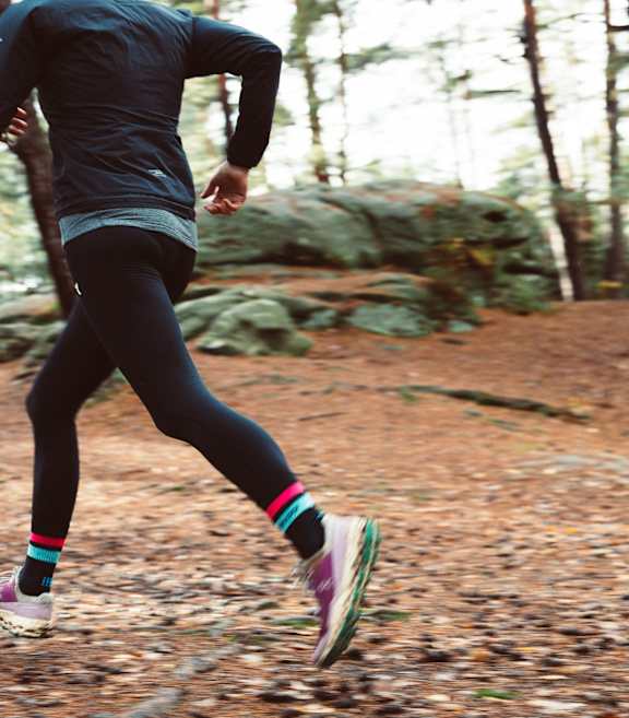A person running in a forest wearing a black top and black leggings.