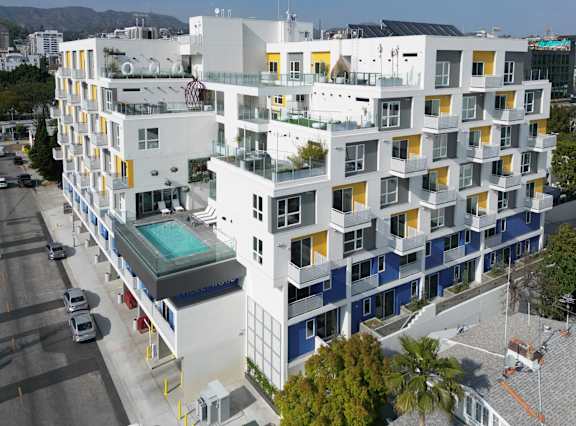 an aerial view of a white building with blue and yellow windows and a pool in front of