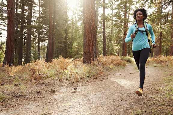 A woman is running on a trail in the woods.