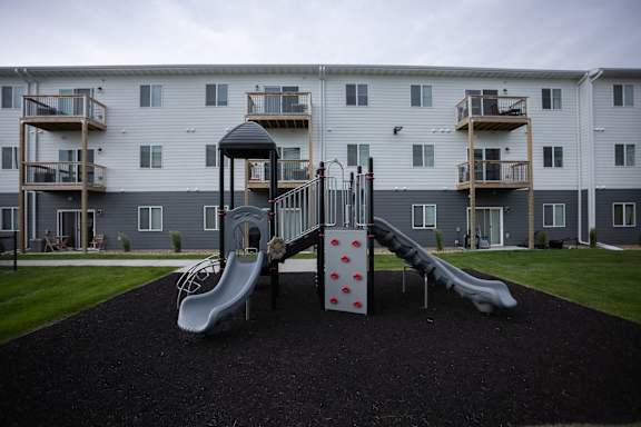 A playground with a slide and a climbing frame in front of a building.