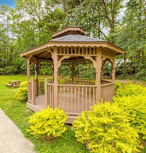 A gazebo is surrounded by bushes and a concrete walkway.