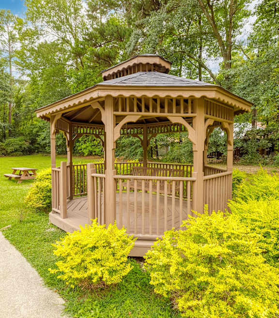 A gazebo is surrounded by bushes and a concrete walkway.