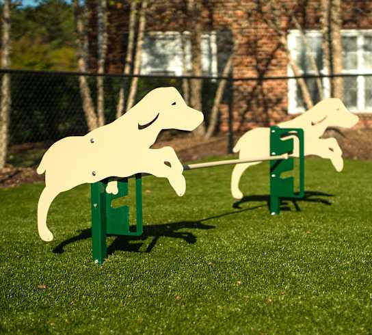Two wooden dog sculptures are on green stands in a grassy area.