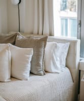 A comfortable bed with white pillows in a well-lit room, featuring a window that brings in natural light.