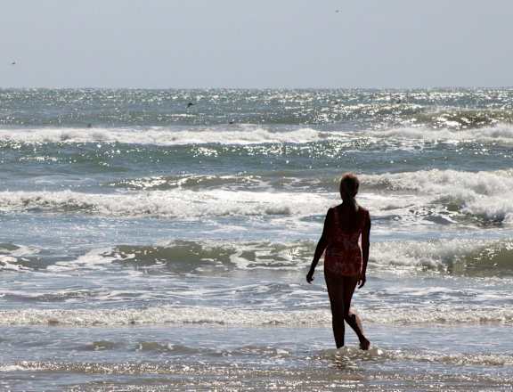 A person is walking along the shore of a beach.