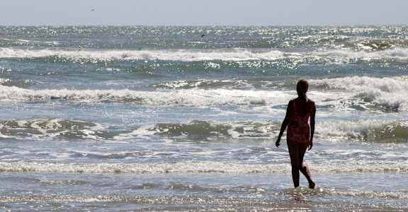 A person is walking along the shore of a beach.