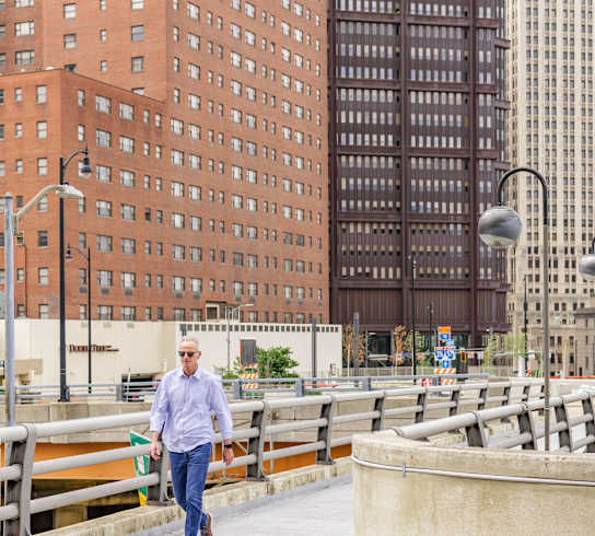 a man walking across a bridge in front of tall buildings at The Washington at Chatham, Pittsburgh Pennsylvania