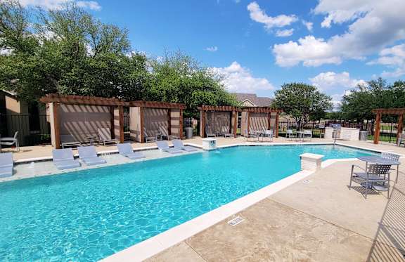 A large swimming pool surrounded by lounge chairs and wooden fences.