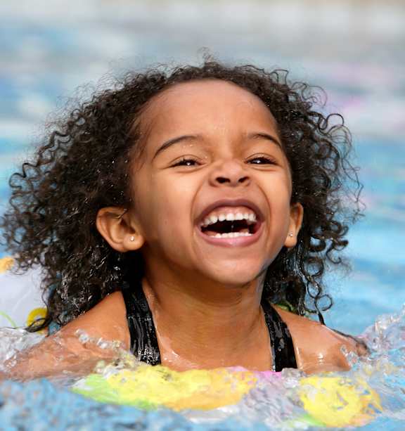 A young girl with curly hair is swimming in a pool.