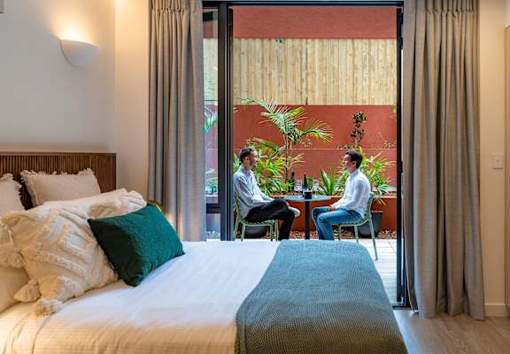 two men sitting at a table in a hotel room with a bed