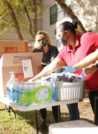 two women wearing masks and gloves donating food to a box