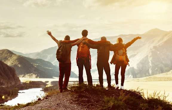 Three people stand on a mountain with their arms outstretched.