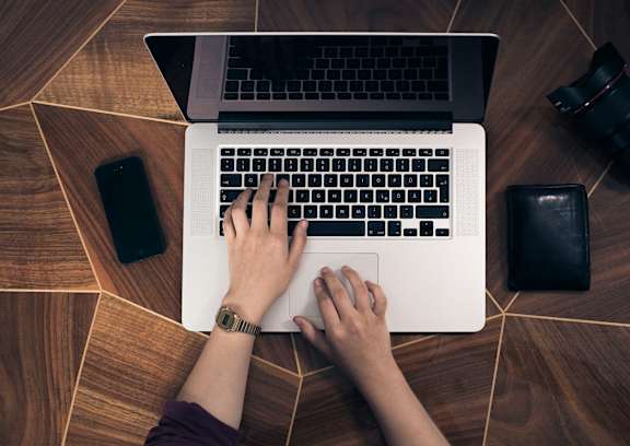 A person is typing on a laptop with a black keyboard.
