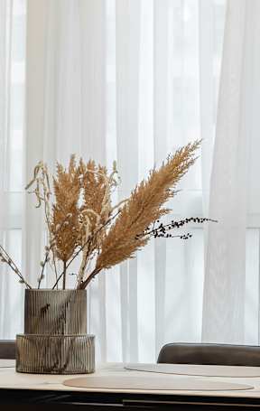 A table with a vase of dried plants on it.