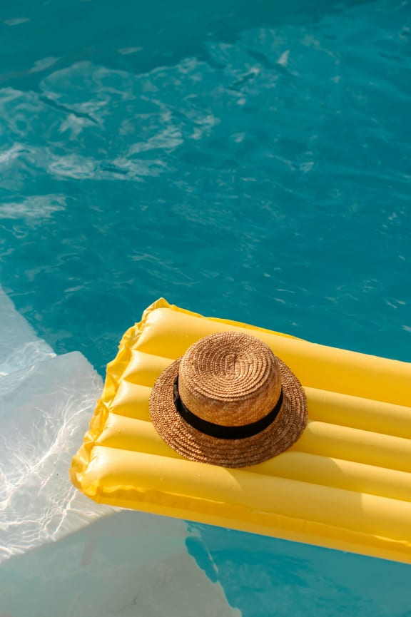a straw hat is sitting on a yellow raft in a pool