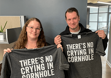 two people holding up t shirts that read there is no crying in cornhole