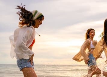 Three people are running and splashing in the ocean.