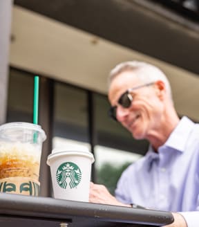 a man sitting at a table with two cups of starbucks coffee