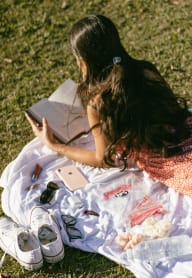 a woman sitting on the grass reading a book