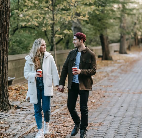 a man and a woman walking down a path holding drinks