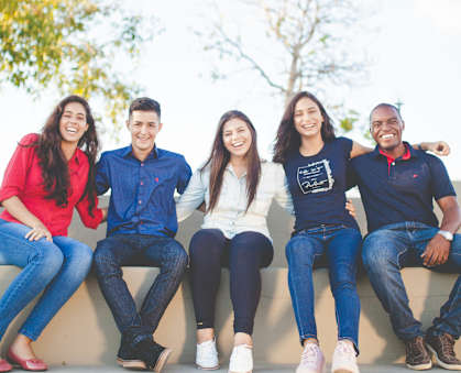 Five people are sitting on a wall outside.