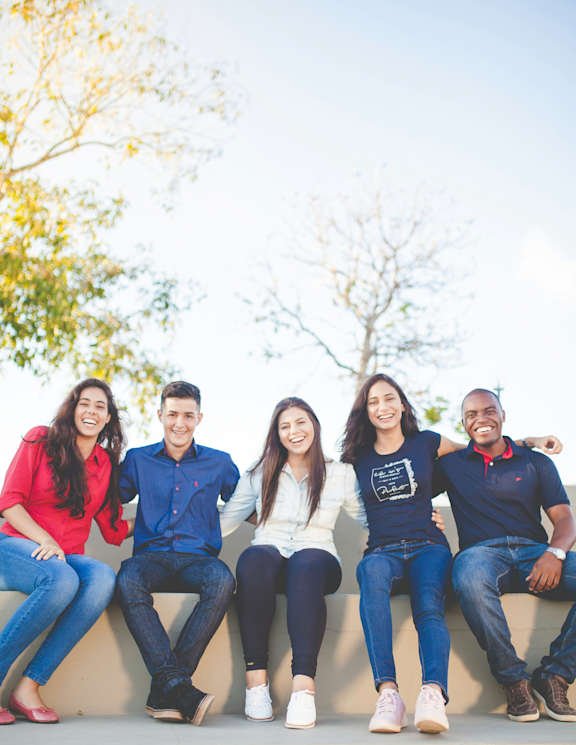 Five people are sitting on a wall outside.