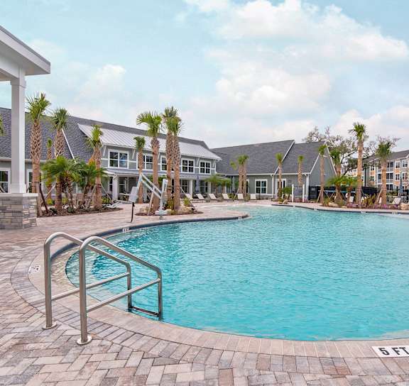 A large outdoor swimming pool surrounded by palm trees and a stone wall.
