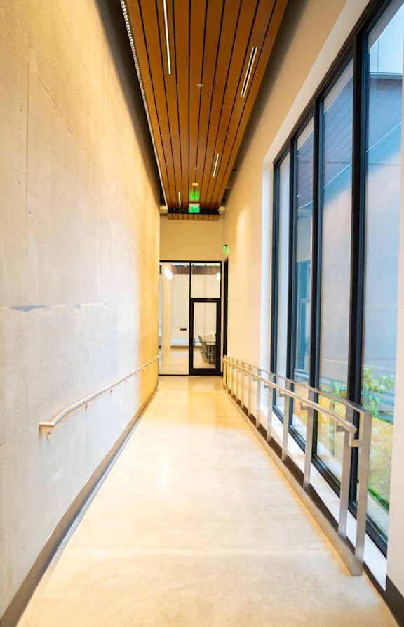 a corridor in a building with large windows and a wooden ceiling