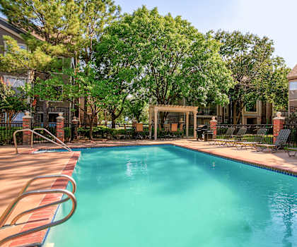 A swimming pool surrounded by trees and chairs.