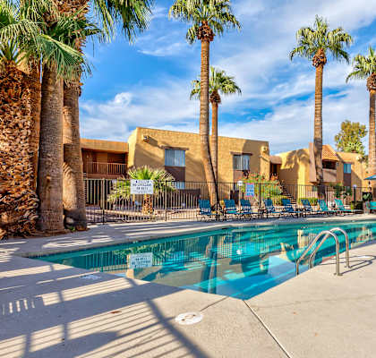 A pool surrounded by palm trees and a building in the background.