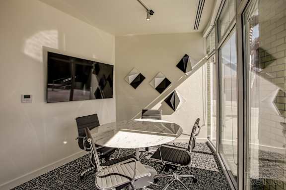 A conference room with a table and chairs and a wall-mounted monitor.