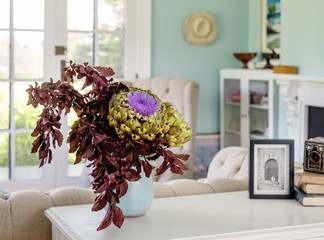 A vase with purple and green flowers on a white table.