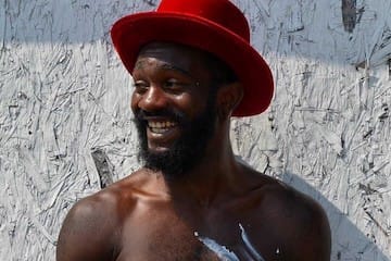 Artist Dewon Moton wearing a bright red hat and smiling with paint on his bare chest at The Citizen Birmingham