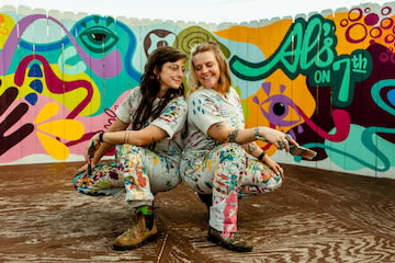 Artists Jordy and Levi of Bendy Knees Design wearing paint covered clothes and squatting in front of a mural at The Citizen Birmingham