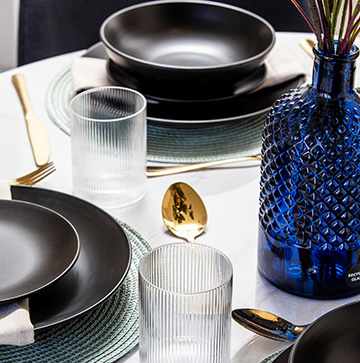 A table set with black plates, glasses, and a blue vase.