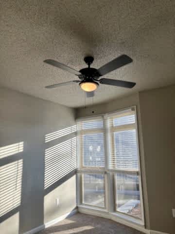 A room with a ceiling fan and a window with blinds.