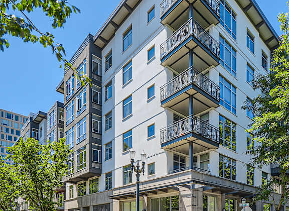 A street view of a multi-story building with balconies and a clear blue sky above.