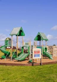 a playground with a large green playset in a park