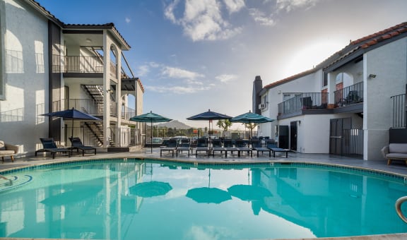 a large swimming pool with chairs and umbrellas in front of a building