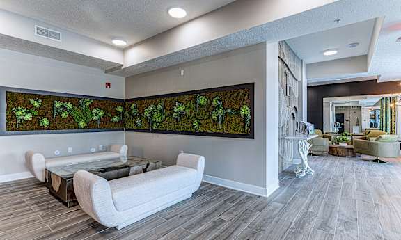 A living room with a grey floor and a large painting of green plants on the wall.