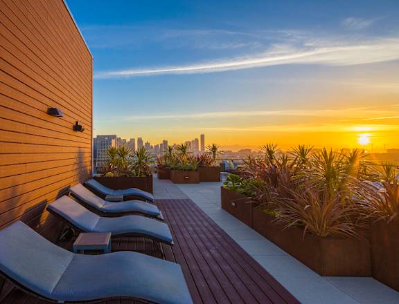 A sunset view from a rooftop patio with lounge chairs and plants.