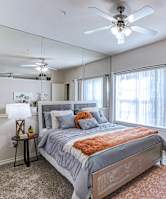 A bedroom with a bed, a ceiling fan, and a mirror.