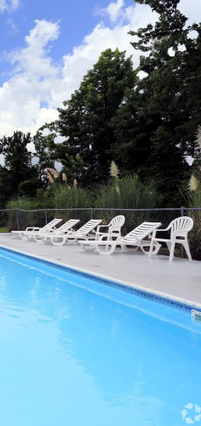 a swimming pool with white chairs and a fence around it