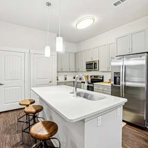 A white kitchen with a refrigerator, sink, and bar stools.