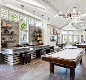 A billiard table is in the middle of a room with a kitchen area to the left.