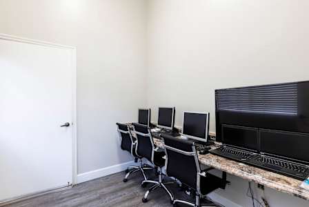 A room with a desk, chairs, and computer monitors.